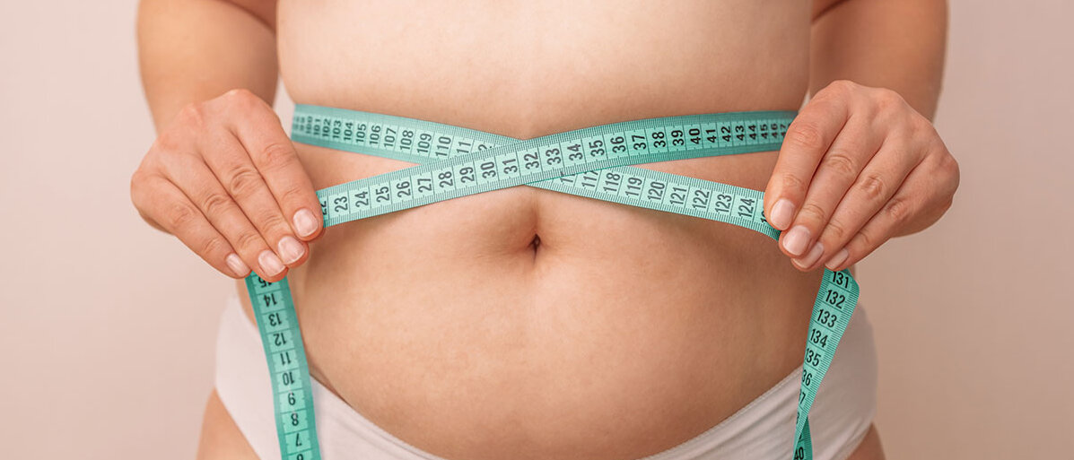 Übergewichtige Frau misst ihren Bauchumfang mit einem Maßband.